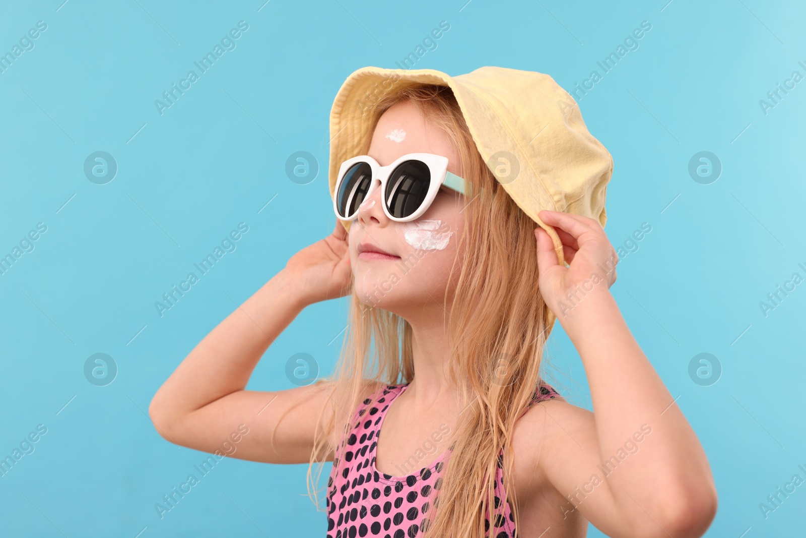 Cute little girl with sun protection cream on her face against light blue background Photo of Cute little girl with sun protection cream on her face against light blue background