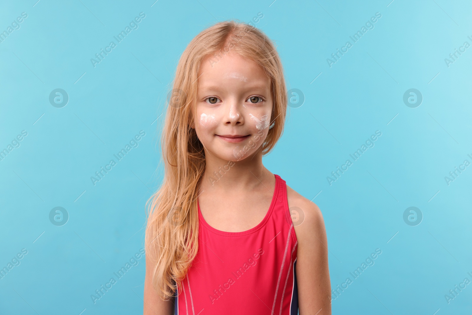 Cute little girl with sun protection cream on her face against light blue background Photo of Cute little girl with sun protection cream on her face against light blue background