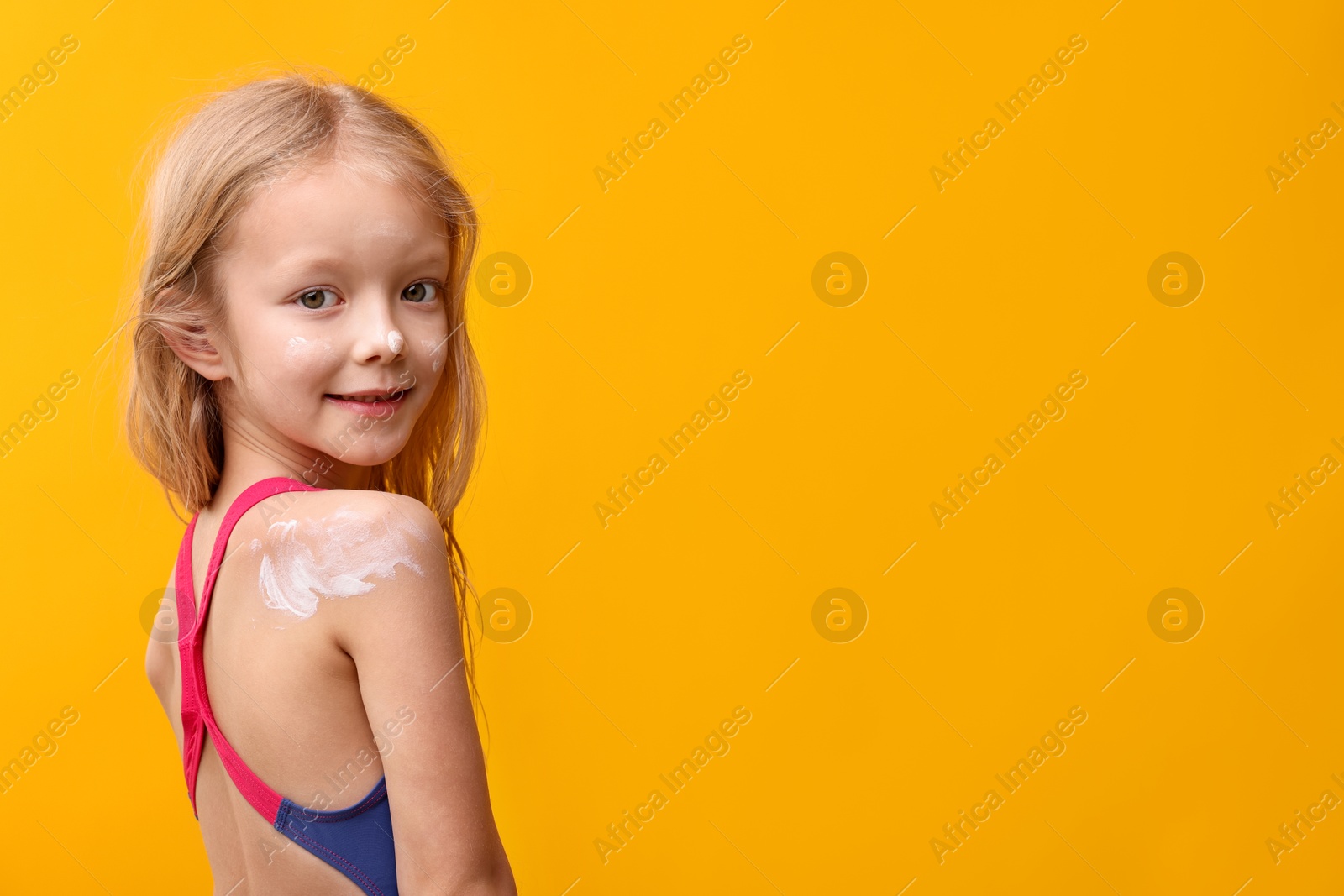 Cute little girl with sun protection cream on her skin against yellow background. Space for text Photo of Cute little girl with sun protection cream on her skin against yellow background. Space for text