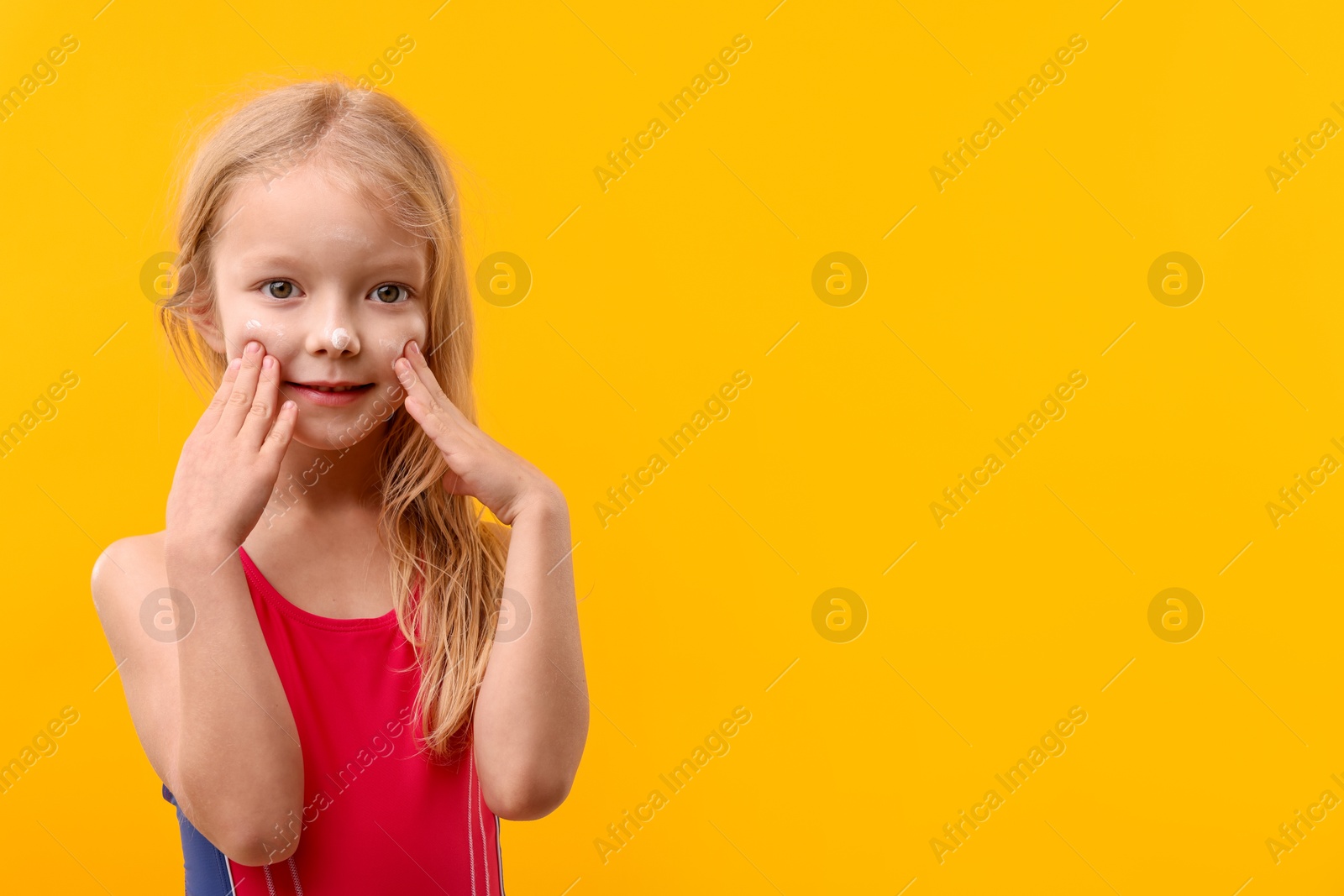 Photo of Cute little girl applying sun protection cream onto her face against yellow background. Space for text