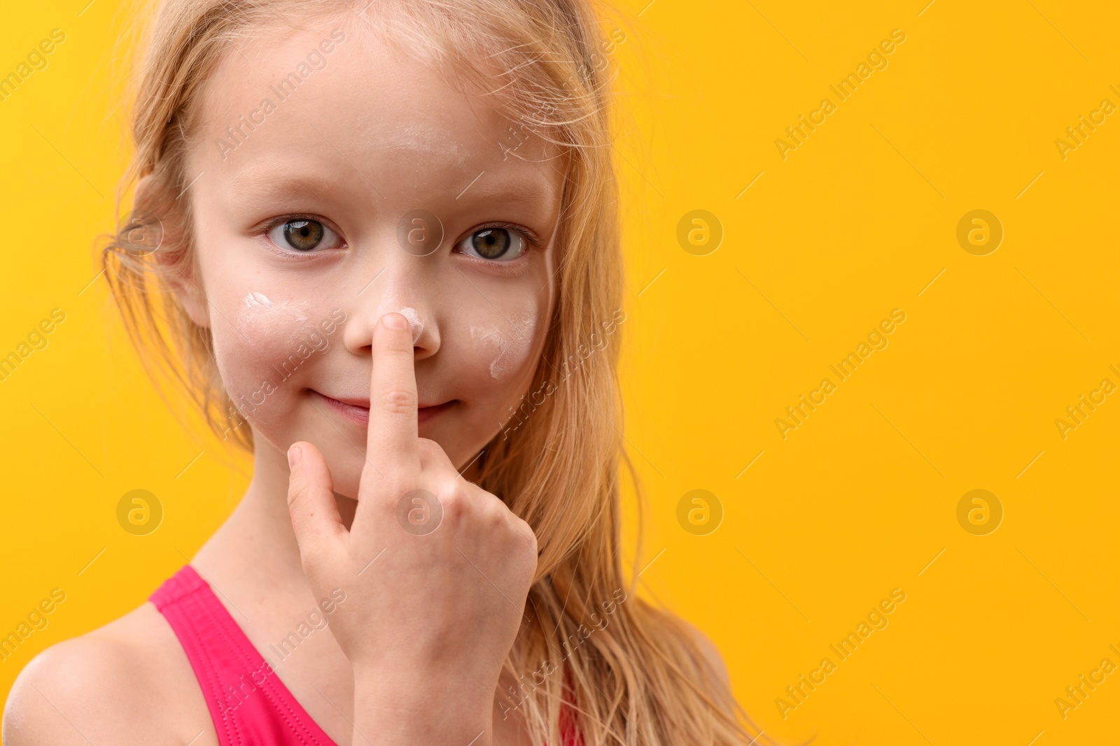 Cute little girl applying sun protection cream onto her nose against yellow background, closeup. Space for text Photo of Cute little girl applying sun protection cream onto her nose against yellow background, closeup. Space for text