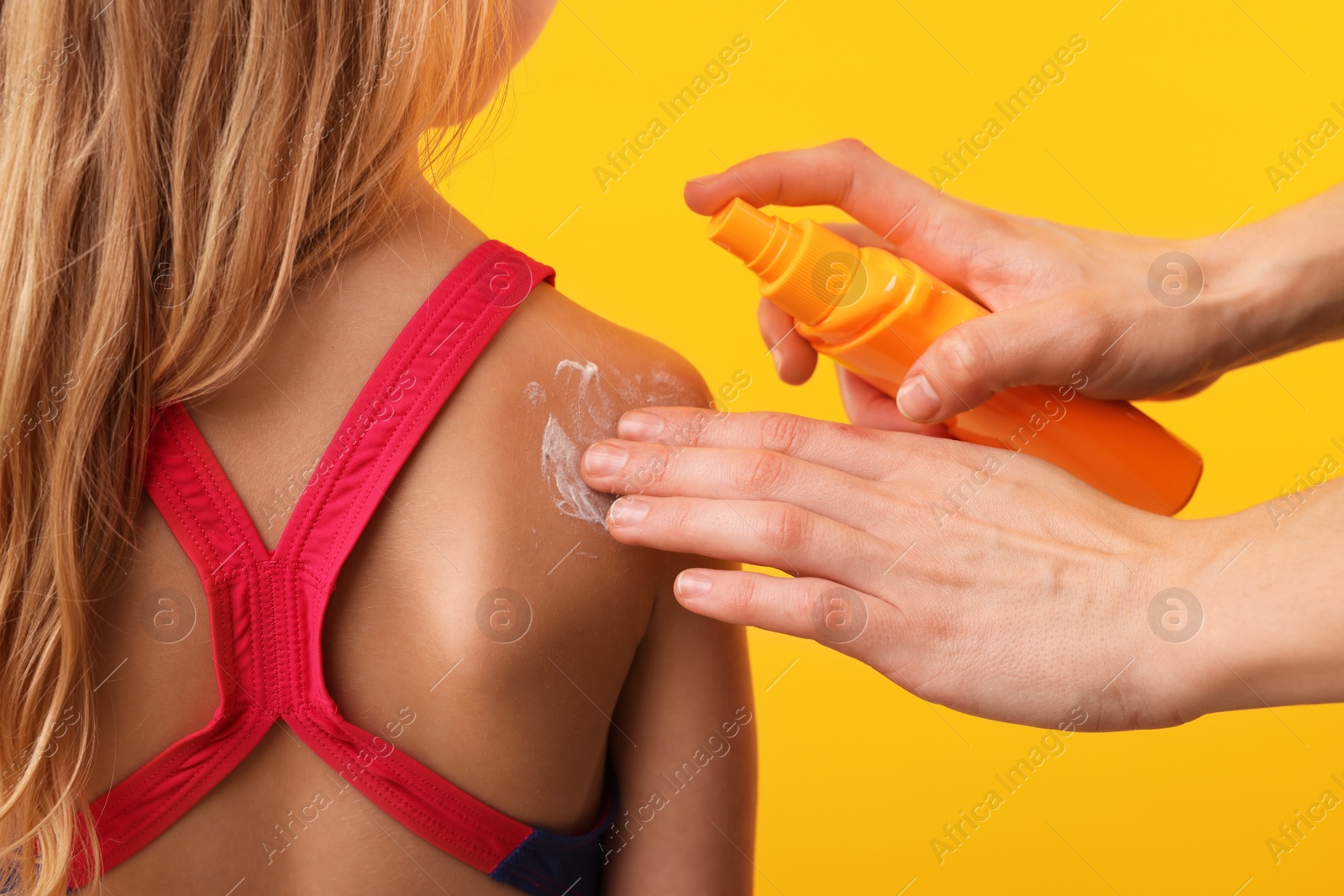 Mother applying sun protection product onto her daughter's skin on yellow background, closeup Photo of Mother applying sun protection product onto her daughter's skin on yellow background, closeup
