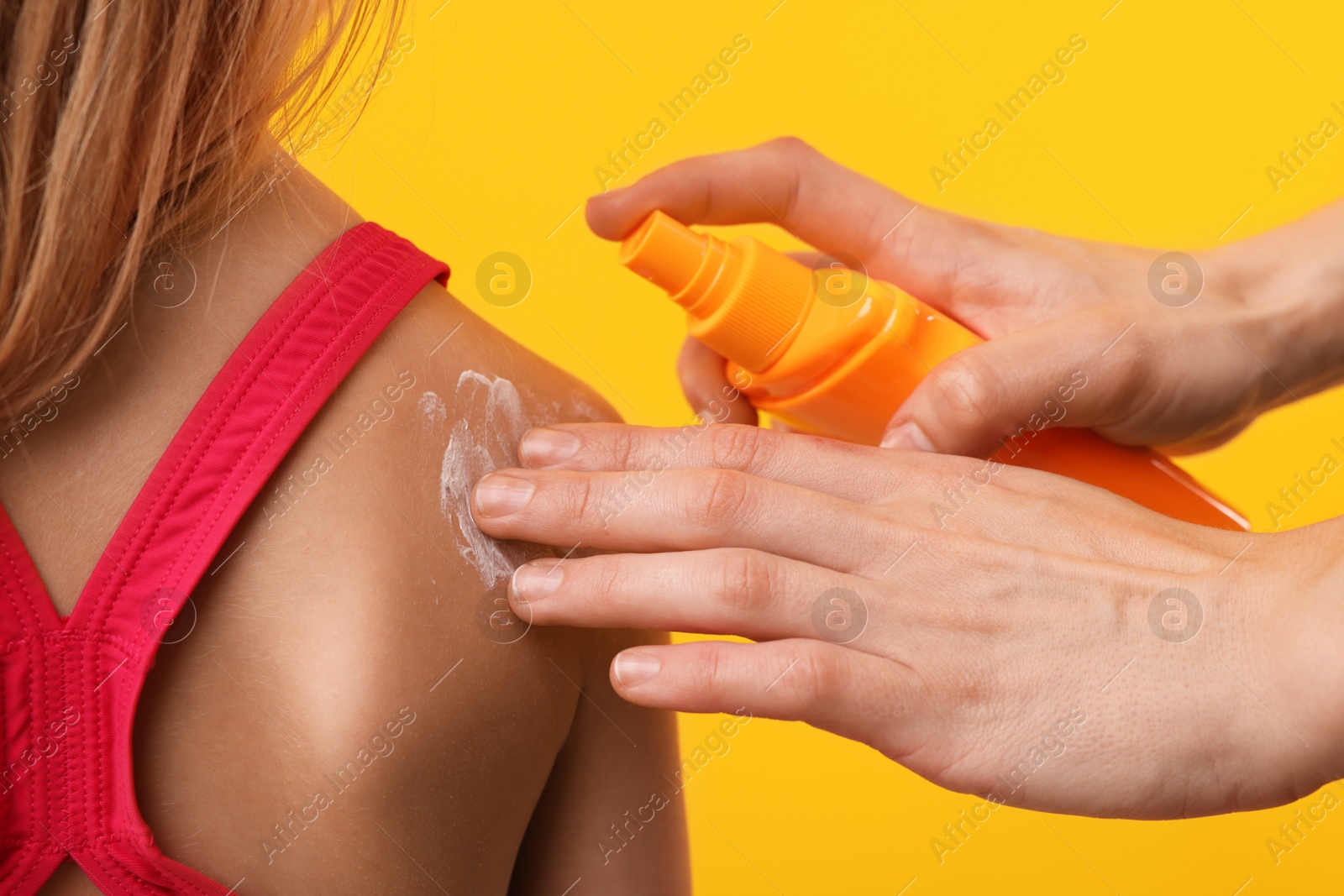 Mother applying sun protection product onto her daughter's skin on yellow background, closeup Photo of Mother applying sun protection product onto her daughter's skin on yellow background, closeup