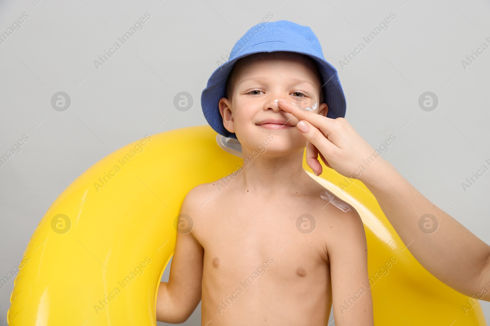 Mother applying sun protection cream onto her son's skin on light grey background, closeup Photo of Mother applying sun protection cream onto her son's skin on light grey background, closeup