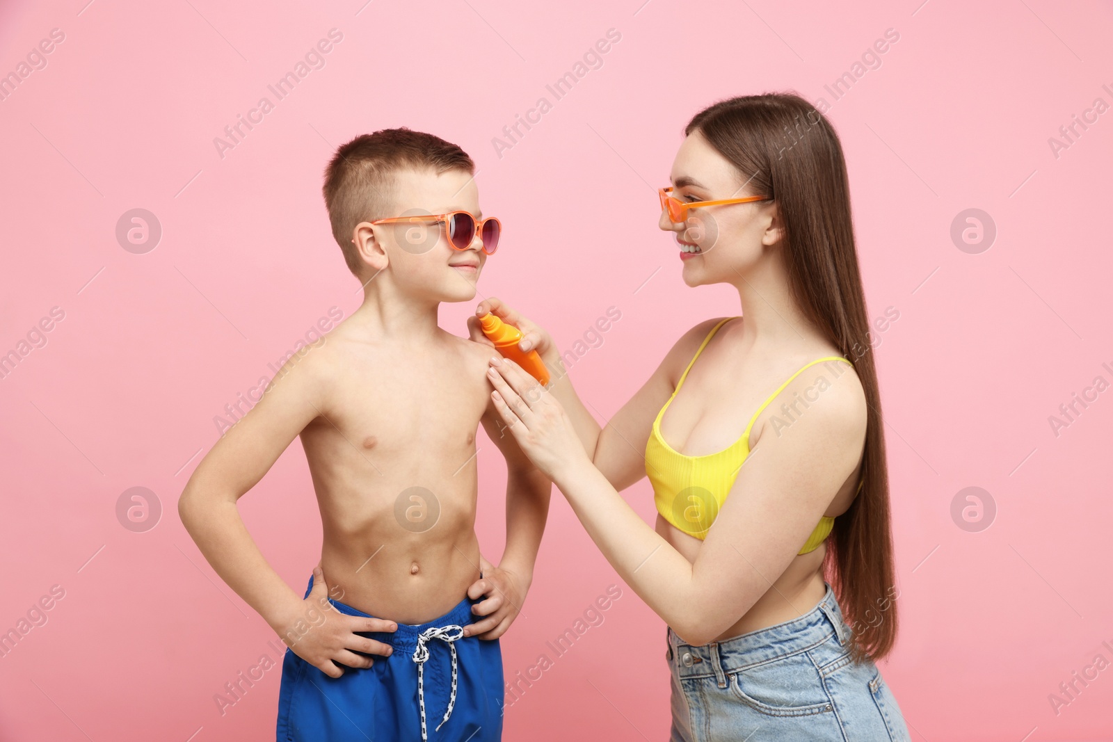 Photo of Mother applying sun protection cream onto her son's skin on pink background