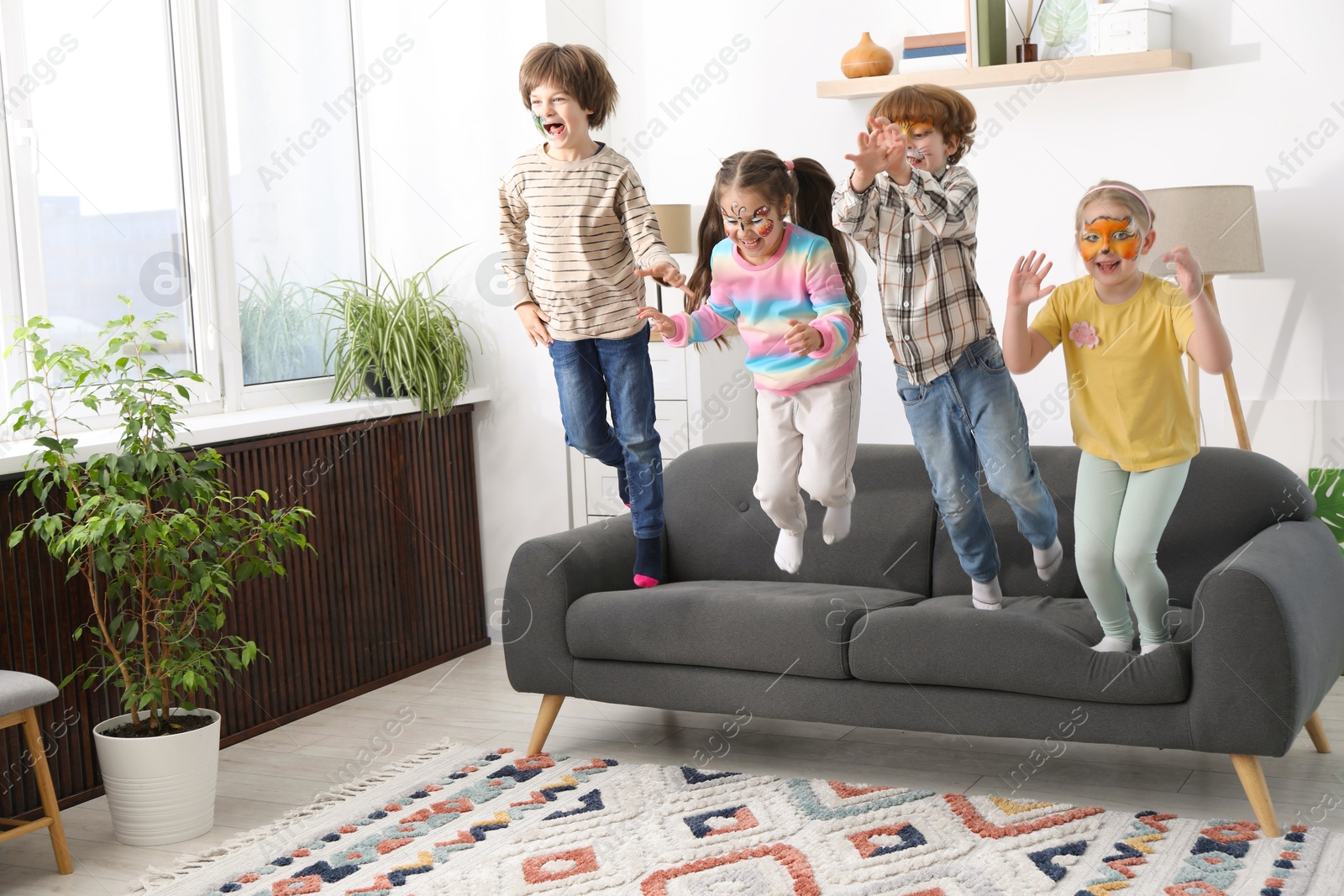 Group of kids with colorful face paintings jumping on sofa indoors Photo of Group of kids with colorful face paintings jumping on sofa indoors