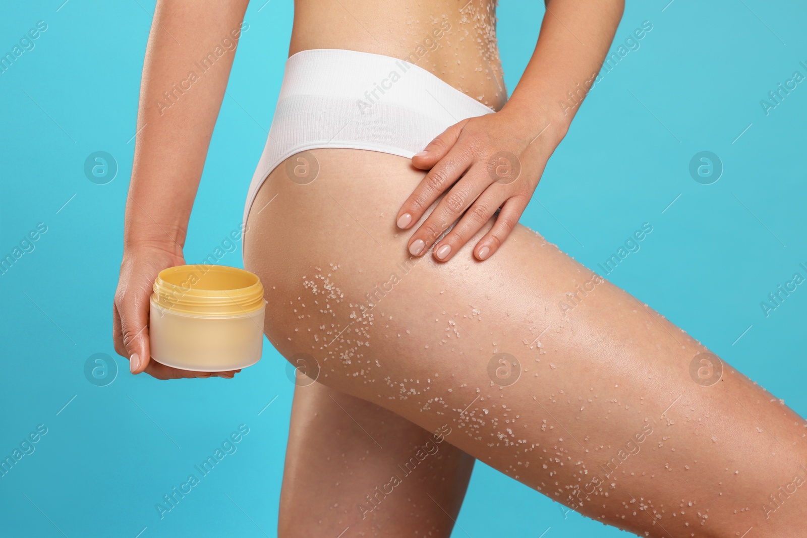 Woman with body scrub on her skin and jar against light blue background, closeup Photo of Woman with body scrub on her skin and jar against light blue background, closeup