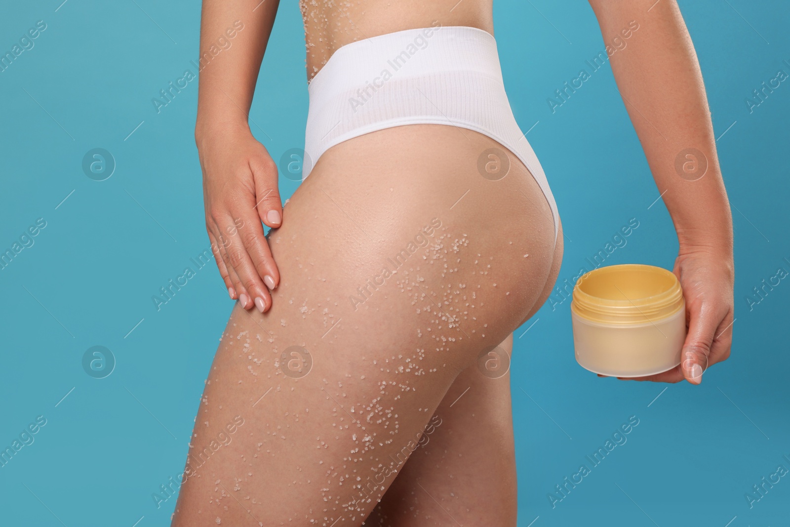 Photo of Woman with body scrub on her skin and jar against light blue background, closeup