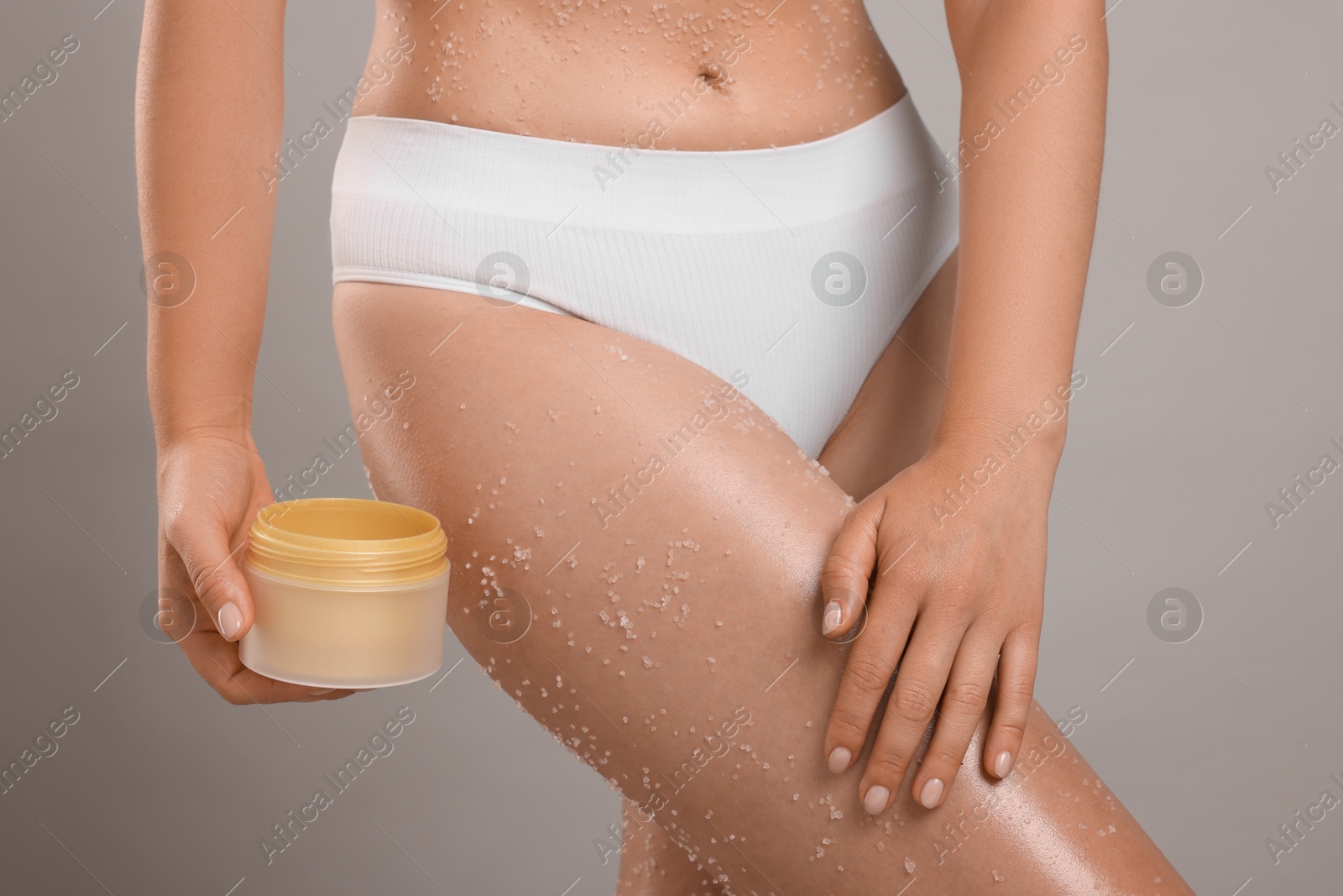 Photo of Woman with body scrub on her skin and jar against grey background, closeup
