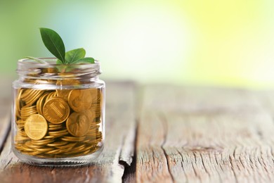 Photo of Investment concept. Glass jar with coins and sprout on wooden table against blurred green background, space for text