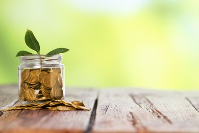 Photo of Investment concept. Glass jar with coins and sprout on wooden table against blurred green background, space for text