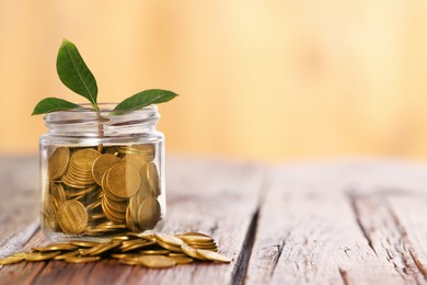 Photo of Investment concept. Glass jar with coins and sprout on wooden table against blurred orange background, space for text