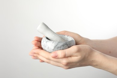 Photo of Woman with mortar and pestle on light background, closeup