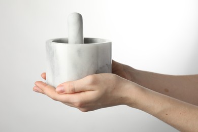 Photo of Woman with mortar and pestle on light background, closeup