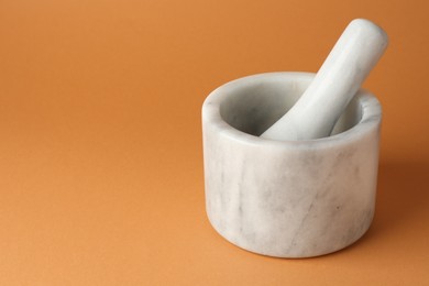 Photo of Marble mortar and pestle on light brown background, closeup. Space for text