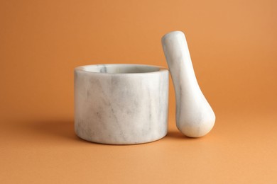 Photo of Marble mortar and pestle on light brown background, closeup