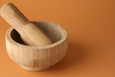Photo of Wooden mortar and pestle on light brown background, closeup. Space for text