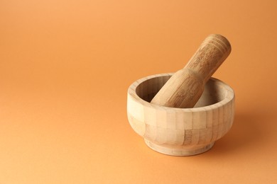 Photo of Wooden mortar and pestle on light brown background, closeup. Space for text