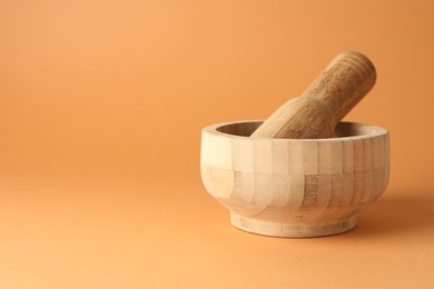 Photo of Wooden mortar and pestle on light brown background, closeup. Space for text