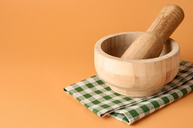 Photo of Wooden mortar, pestle and cloth on light brown background, closeup. Space for text