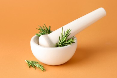 Photo of Ceramic mortar with rosemary and pestle on light brown background, closeup