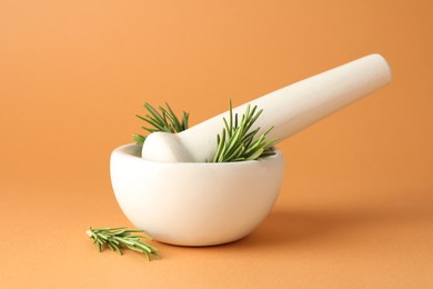 Photo of Ceramic mortar with rosemary and pestle on light brown background, closeup