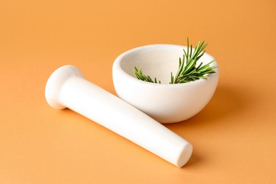 Photo of Ceramic mortar with rosemary and pestle on light brown background, closeup