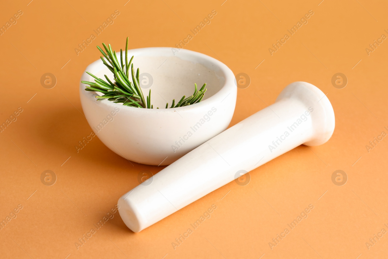 Photo of Ceramic mortar with rosemary and pestle on light brown background, closeup