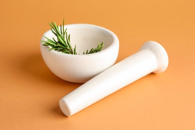 Photo of Ceramic mortar with rosemary and pestle on light brown background, closeup
