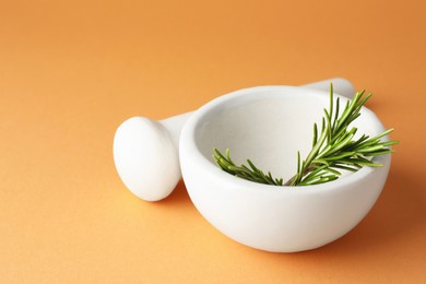 Photo of Ceramic mortar with rosemary and pestle on light brown background, closeup