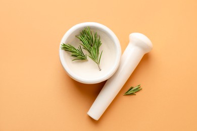 Photo of Ceramic mortar with rosemary and pestle on light brown background, top view