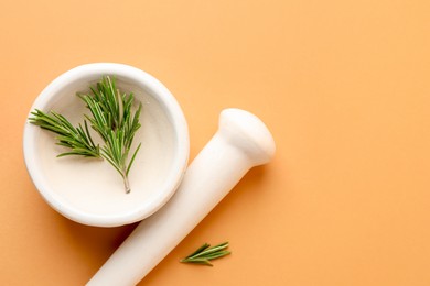 Photo of Ceramic mortar with rosemary and pestle on light brown background, top view. Space for text