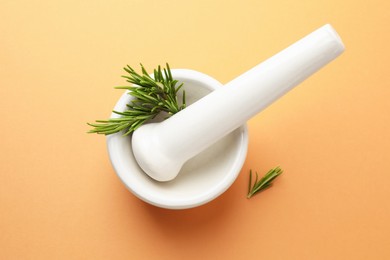 Photo of Ceramic mortar with rosemary and pestle on light brown background, top view