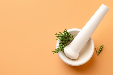 Photo of Ceramic mortar with rosemary and pestle on light brown background, top view. Space for text