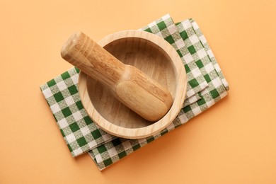 Photo of Wooden mortar, pestle and cloth on light brown background, top view