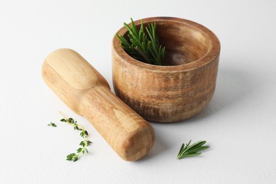 Photo of Wooden mortar with rosemary, thyme and pestle on white table, closeup