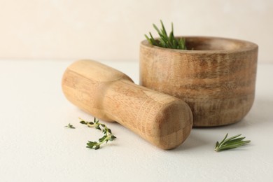 Photo of Wooden mortar with rosemary, thyme and pestle on white table, closeup