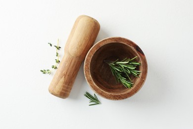 Photo of Wooden mortar with rosemary, thyme and pestle on white table, flat lay