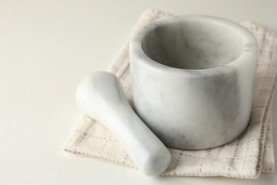 Photo of Marble mortar, pestle and cloth on white table, closeup
