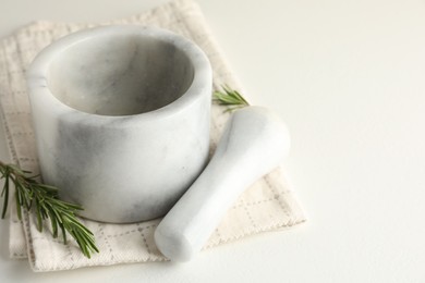 Photo of Marble mortar with rosemary, pestle and cloth on white table, closeup. Space for text