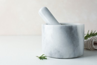 Photo of Marble mortar with rosemary and pestle on white table, closeup. Space for text