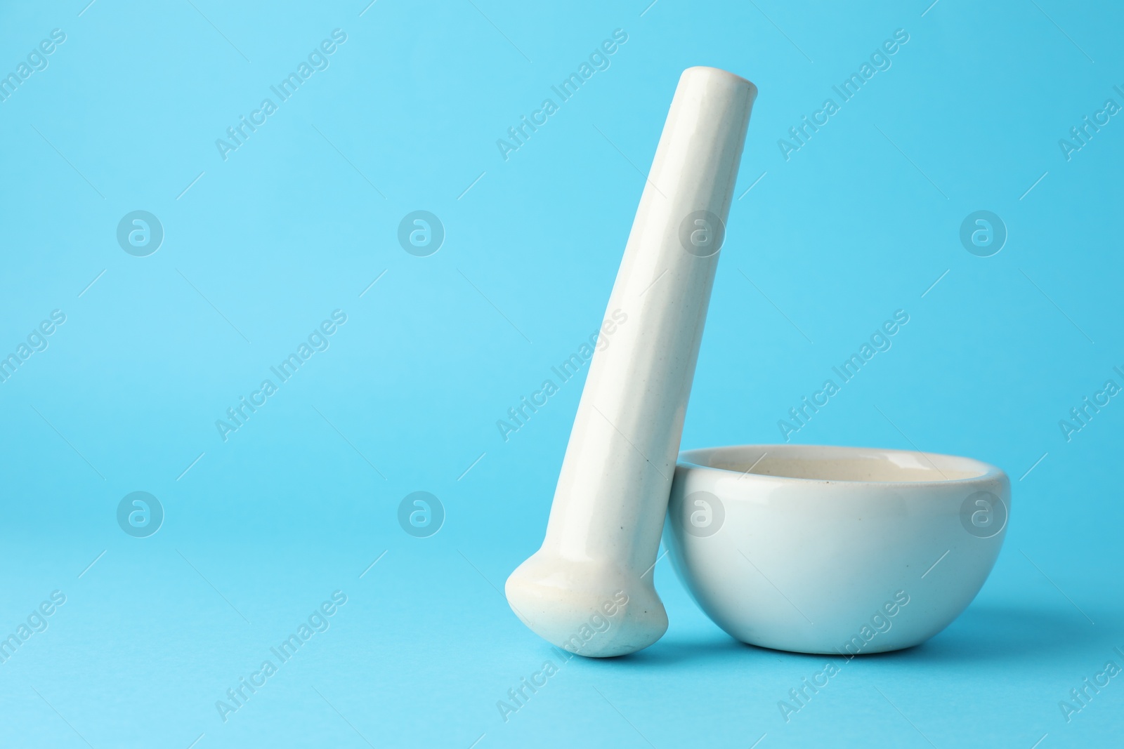Ceramic mortar and pestle on light blue background, closeup. Space for text Photo of Ceramic mortar and pestle on light blue background, closeup. Space for text