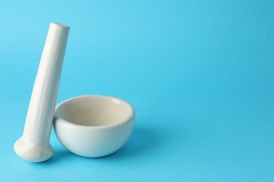Photo of Ceramic mortar and pestle on light blue background, closeup. Space for text