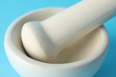 Photo of Ceramic mortar and pestle on light blue background, closeup
