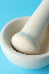 Photo of Ceramic mortar and pestle on light blue background, closeup