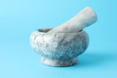 Photo of Marble mortar and pestle on light blue background, closeup
