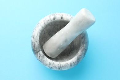 Photo of Marble mortar and pestle on light blue background, top view