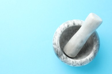 Photo of Marble mortar and pestle on light blue background, top view. Space for text