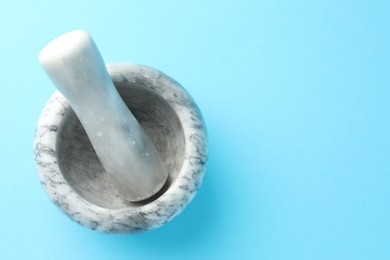 Photo of Marble mortar and pestle on light blue background, top view. Space for text