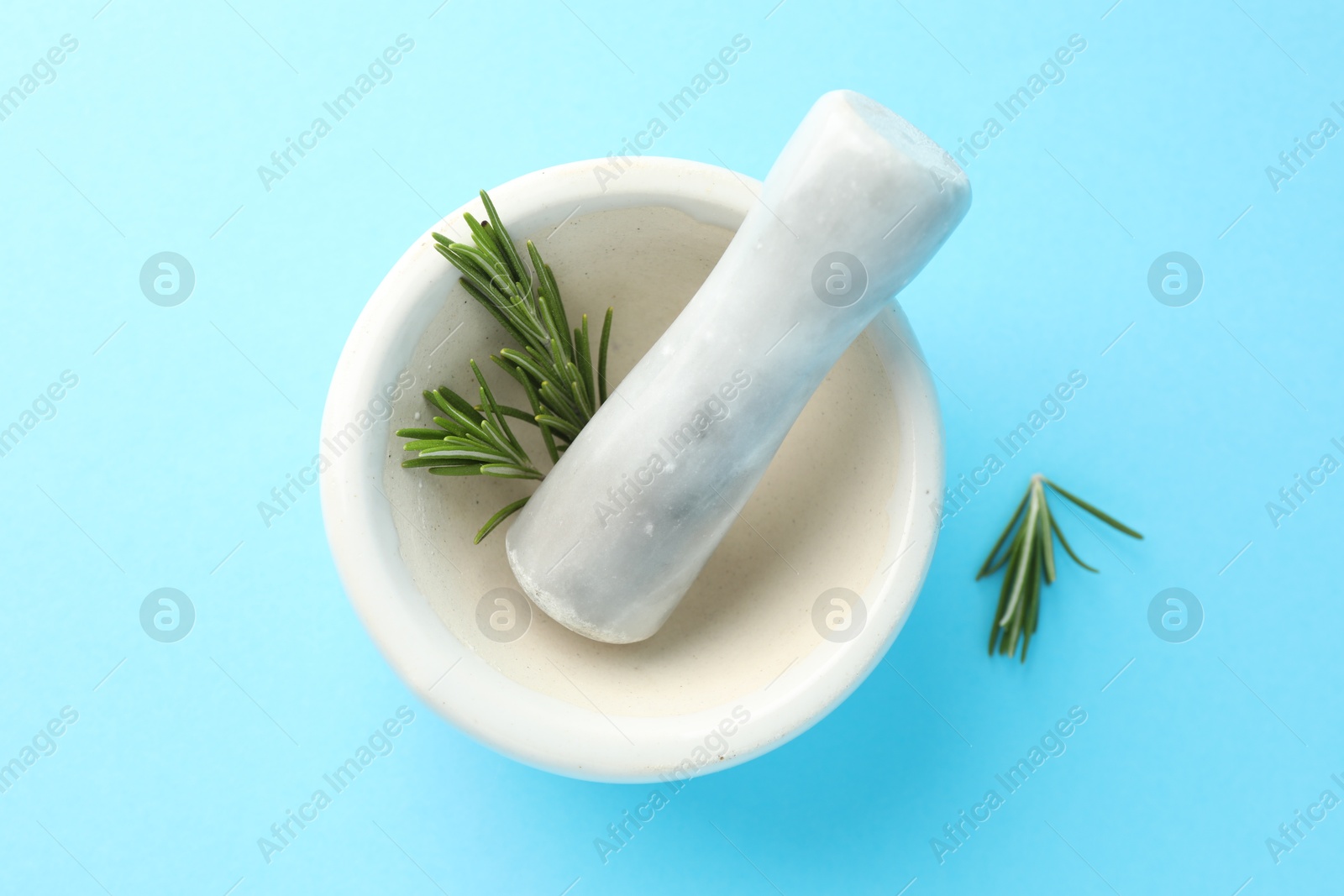 Ceramic mortar with rosemary and pestle on light blue background, top view Photo of Ceramic mortar with rosemary and pestle on light blue background, top view